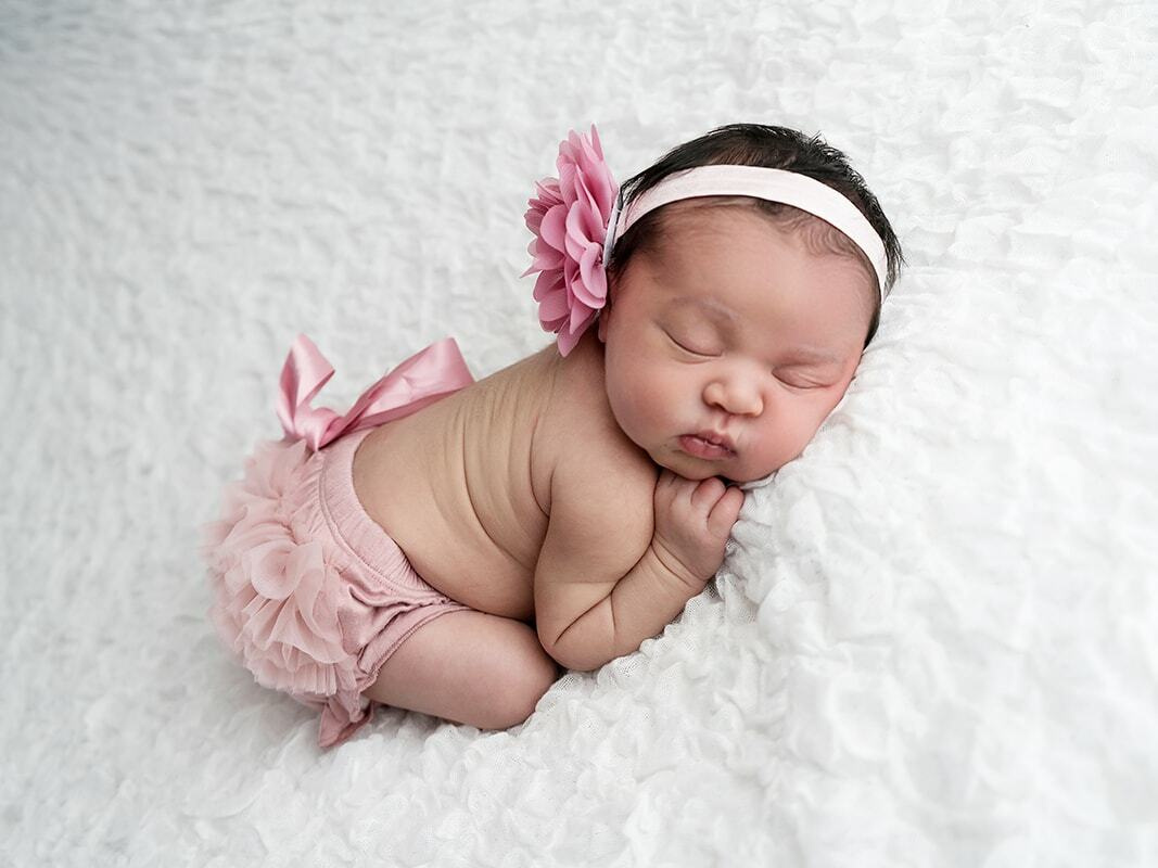 Newborn photoshoot in Croydon Portrait Studio. Baby with pink flower hair band on white blanket