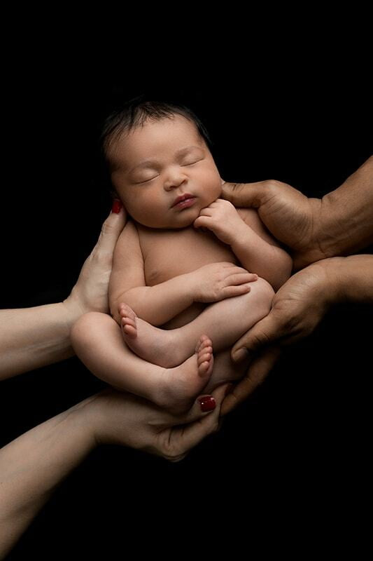 Newborn in both parents hands on black bacground.
