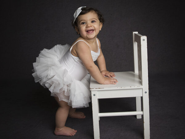 Baby Photoshoot in Croydon portrait studio. Baby standing against chair.