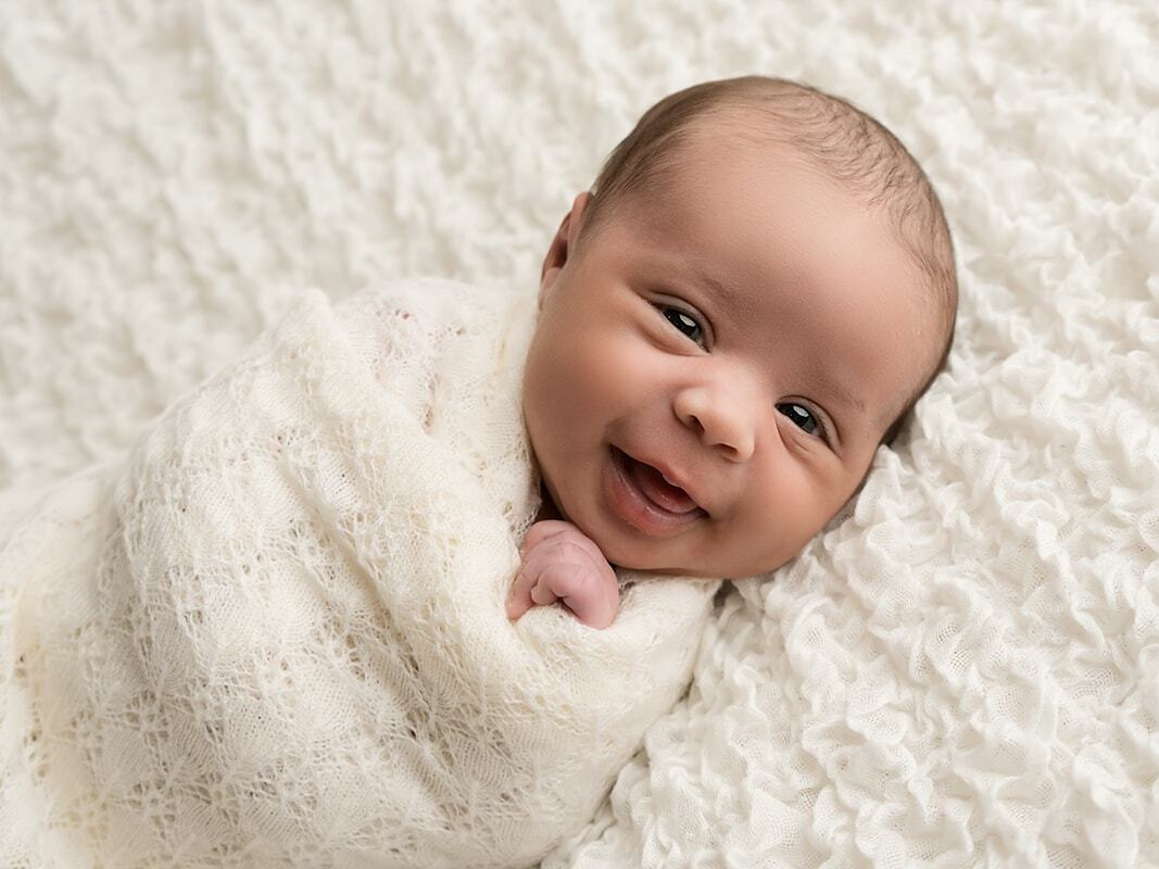 Smiling newborn wrapped in cream blanket. Photoshoot in Croydon studio  